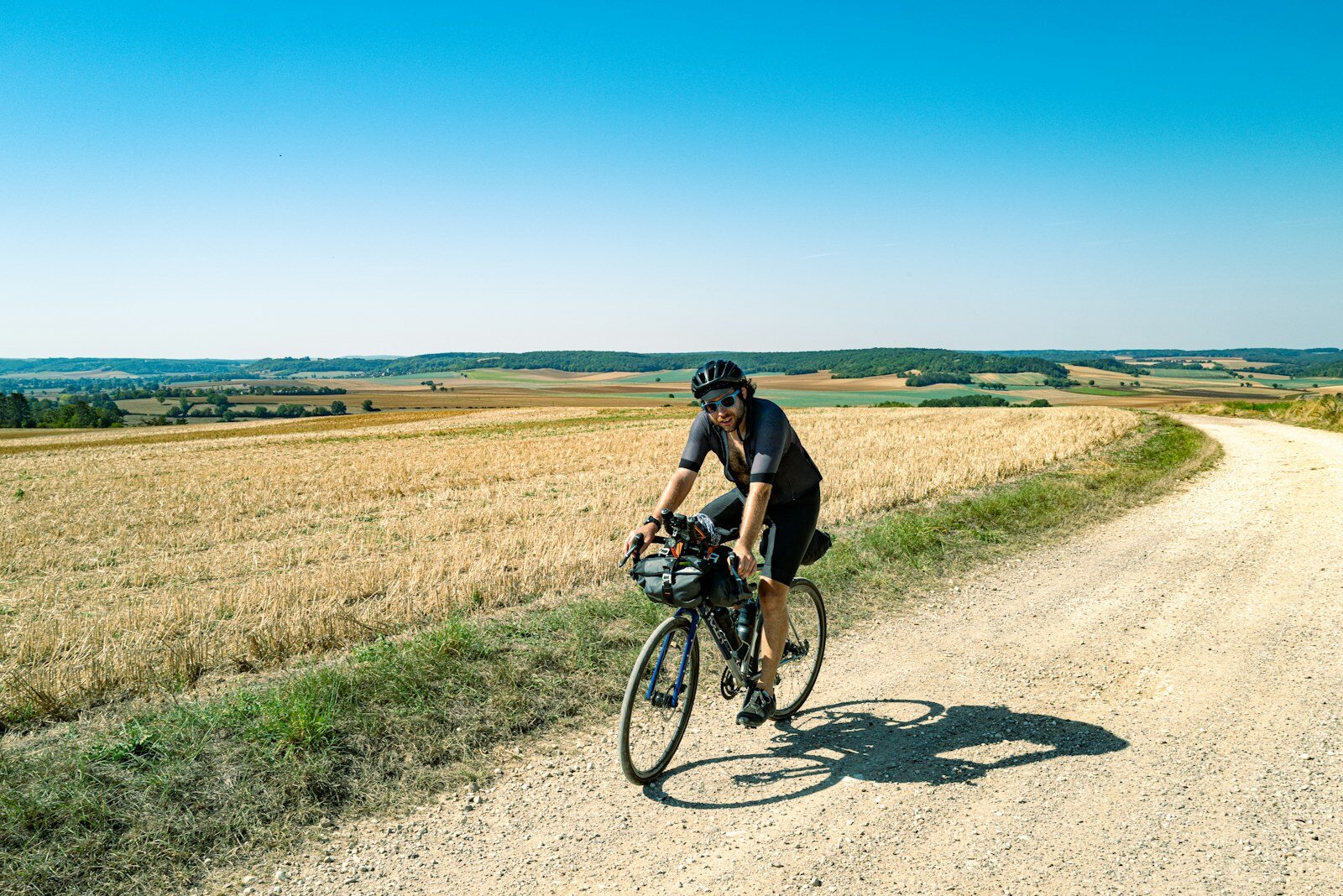 Cycliste gravel roulant sur une piste blanche entre les champs
